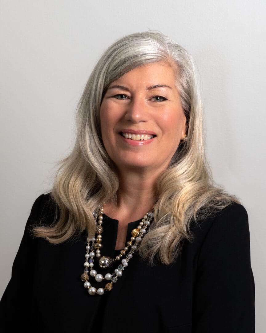 A woman with long white hair wearing black and pearls.